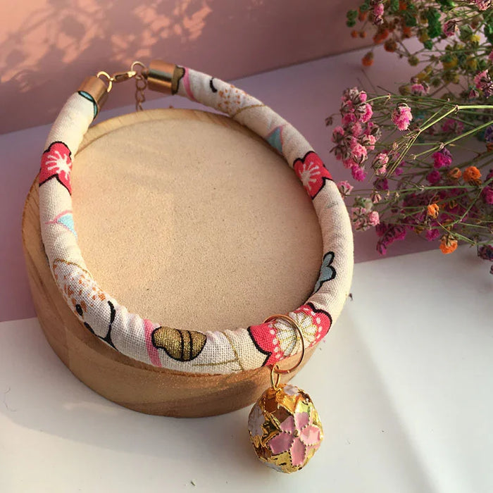Floral patterned pet collar with gold charm, displayed on wooden stand beside dried flowers