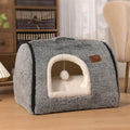 Cozy gray cat bed with plush white interior and hanging pom-pom toy, perfect for indoor pets.