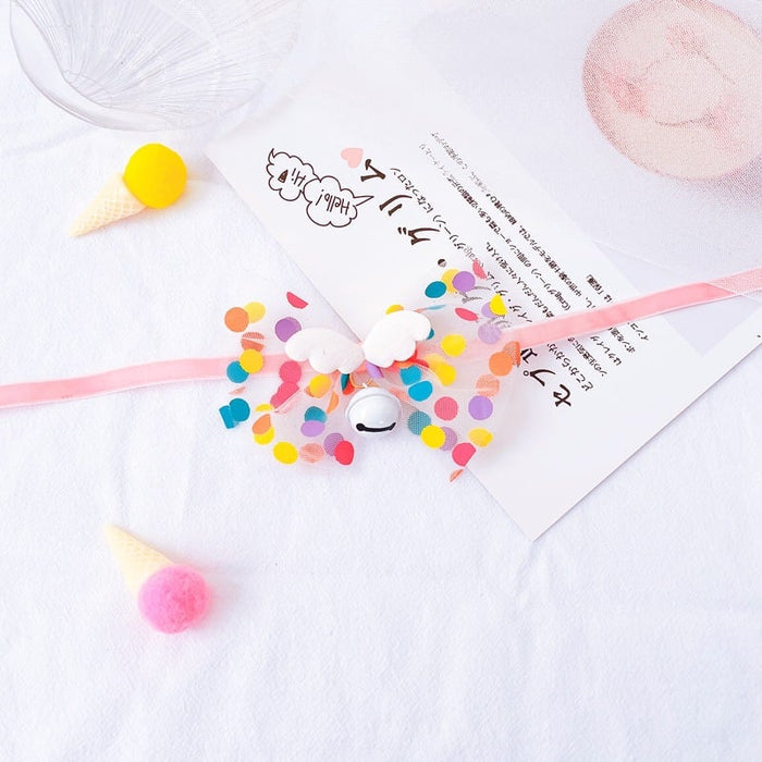 Colorful pet hair bow accessory with pom poms and a small bell on a white background.